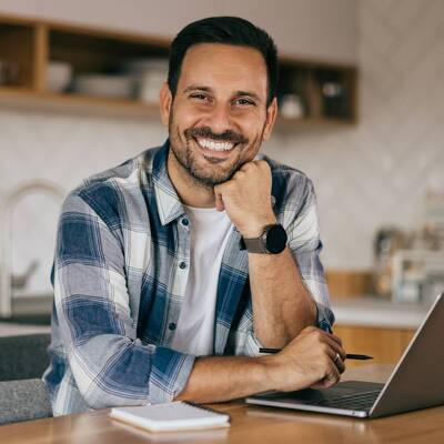 Geschäftsmann sitzt in der Apartmentküche und arbeitet am Laptop.